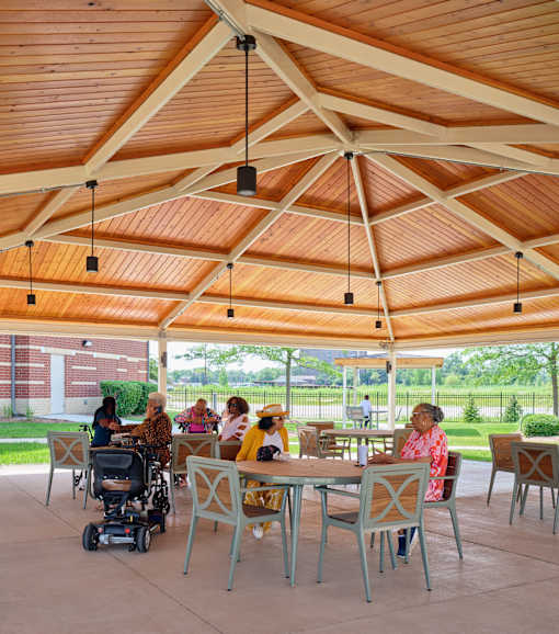 A group of people are sitting at tables under a wooden roof.