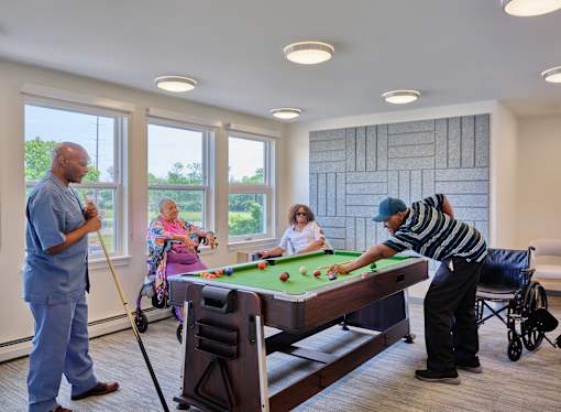 A man in a blue uniform is sweeping the floor while others play pool.