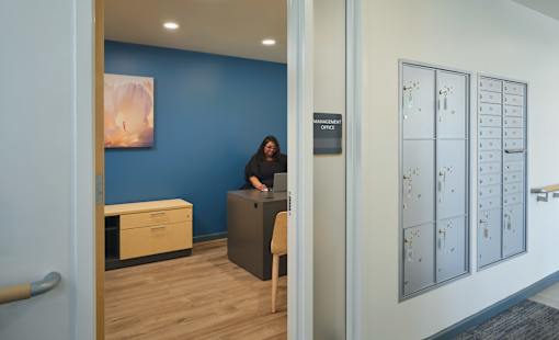 A woman is sitting at a desk in an office with a blue wall behind her.