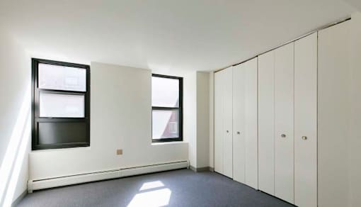 A room with white walls and a grey floor with a row of cupboards on the right.