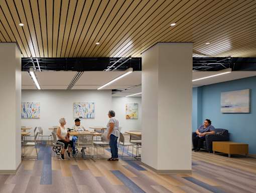 A group of people are sitting and standing in a room with wooden floors and ceiling.