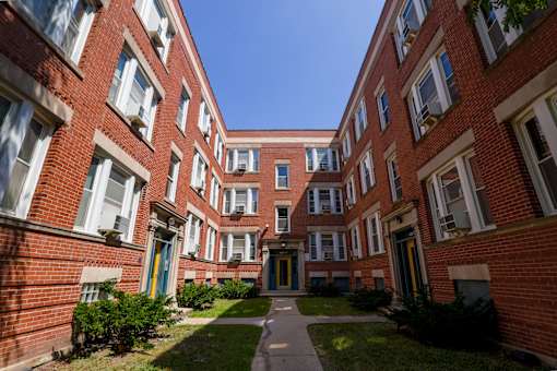 A long hallway with red brick buildings and green bushes on the side.