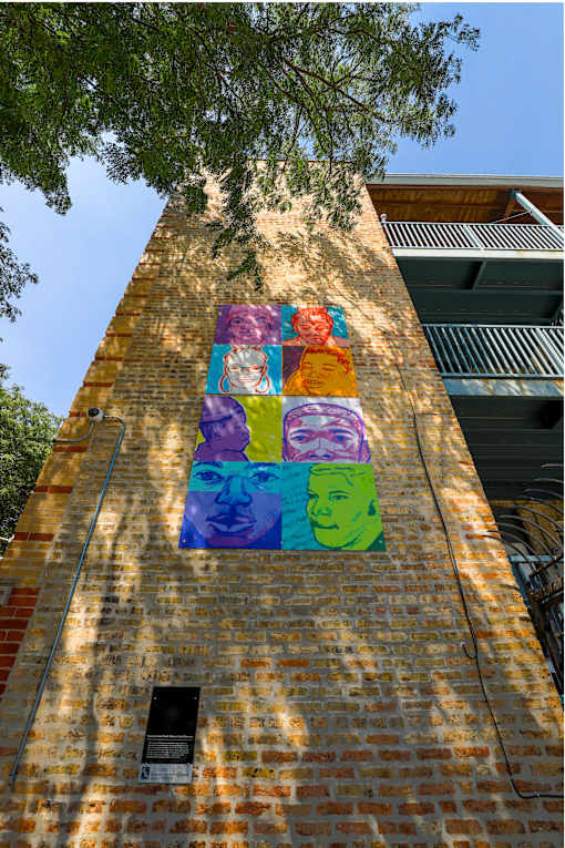 A mural on a brick wall features a face with a purple hat and green hair.