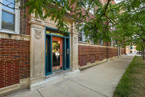 A brick building with a green door and a tree branch in the foreground.