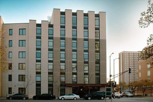 A large building with a lot of windows is in the middle of a street with cars parked in front.