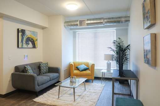 A living room with a grey couch, a yellow chair, a glass table and a plant.