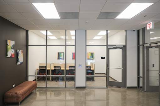 A conference room with a long table and chairs, a bench, and a door with an exit sign above it.