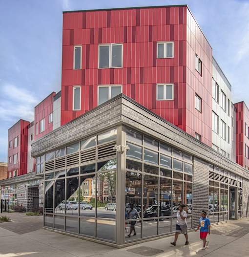 A red building with a large glass front and people walking in front.