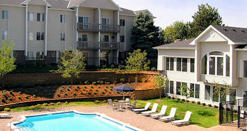 Swimming pool with sundeck and poolside lounge chairs, beautiful landscaping, lush landscaping, apartments with pool view, and park-like setting at Kensington Woods Apartments in Omaha, Nebraska
