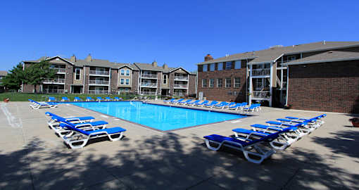 Huge swimming pool with spacious sundeck, poolside lounge chairs, beautiful landscaping, and scenic views at LionsGate Apartments in Lincoln, Nebraska