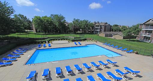 Huge swimming pool with spacious sundeck, poolside lounge chairs, beautiful landscaping, scenic views, lots of trees at LionsGate Apartments in Lincoln, Nebraska