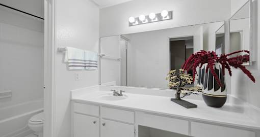 A white bathroom with a sink, mirror, and vase.