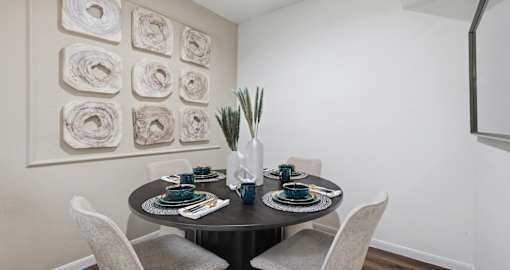 A dining table set with plates and glasses is surrounded by chairs.