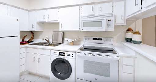 A white kitchen with a washing machine and a microwave.