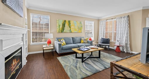 Spacious living room with wood-burning fireplace with glass doors, hardwood floors, and oversized windows Tuscany Park Apartments in Houston.