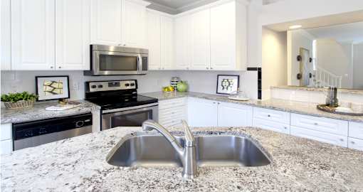 Spacious kitchen with island, granite countertops, white cabinets, smooth glass top stove, spacious pantries, breakfast bar and stainless-steel appliances at Tuscany Villas in Houston.