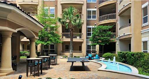 Luxury apartments with palm trees, spacious sundeck with poolside lounge chairs, grilling station, ping-pong table, and fountains at Villa Piana Apartments in Dallas