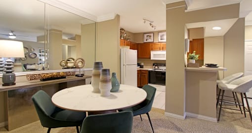 Spacious dining room area with mirror accent wall and kitchen with breakfast bar at Tuscany Lane Apartments in Houston.