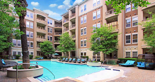 Luxury apartments with resort-style pool, palm trees, spacious sundeck with poolside lounge chairs, grilling station, fountains, and fitness center at Villa Piana Apartments in Dallas