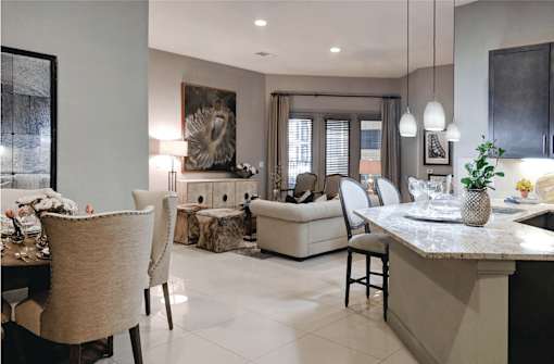 A view of an open living space with a dining nook on the left, kitchen counter on the right, and living area in the front. White furnishing on porcelain floor.