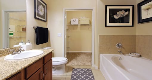 Spacious master bathroom with oval soaking tub, separate glass shower, and attached large walk-in closet at The Voss Apartments in Houston.
