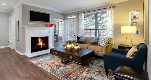 Living room with wood plank floors, gray wall color, wood burning fireplace, oversized window, and built-in shelves.