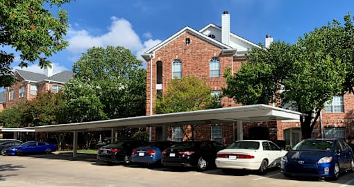 Gated luxury apartment community in north Dallas with red brick exteriors, covered parking, lots of trees, and beautiful landscaping at The Saxony Apartments