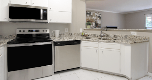 Spacious kitchen with white cabinets, granite countertops, stainless steel appliances, serving bar, and porcelain tile floors at Breckenridge Apartments in southwest Omaha, Nebraska