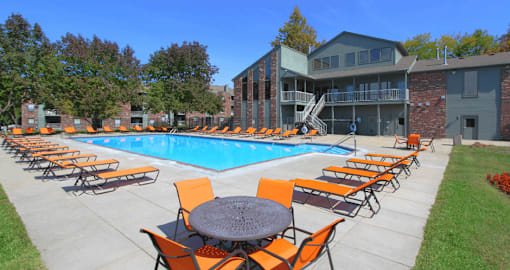 A pool surrounded by orange chairs and tables.