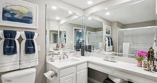 Luxury bathroom with white cabinets, cultured marble vanity, oval soaking tub, and glass shower at The Saxony Apartments in Dallas