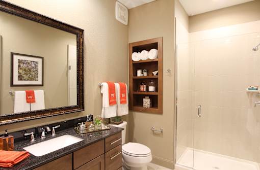 Luxury bath suite with granite slab vanity top, frameless glass walk-in shower, and spacious linen cabinets and built-in shelves at Tuscany Walk Apartments in Houston.