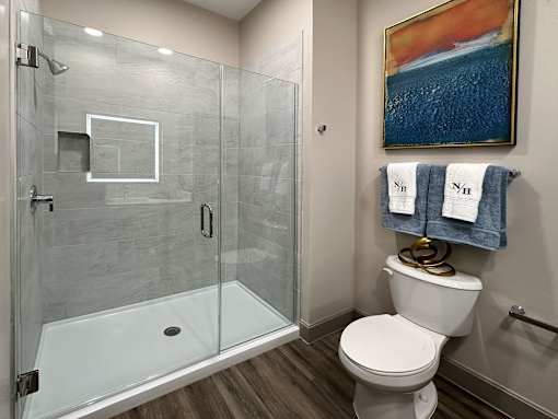 A bathroom with a toilet, a glass shower stall, and a painting on the wall.
