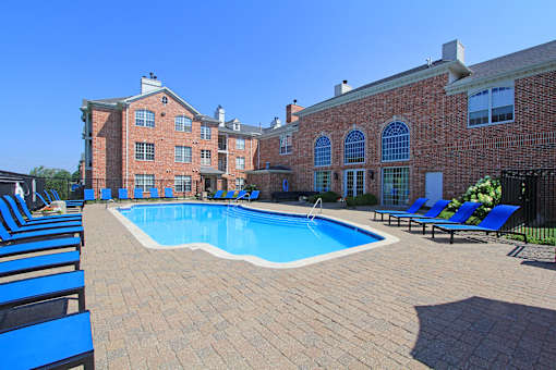 an outdoor pool with blue chairs and a brick building
