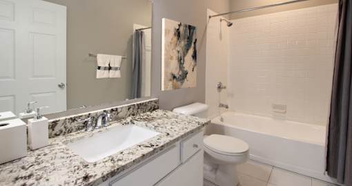 Spacious luxury bathroom with white cabinets, granite countertops, gray wall color, porcelain tile floor, soaking tub and tiled shower at Breckenridge Apartments in Omaha, Nebraska