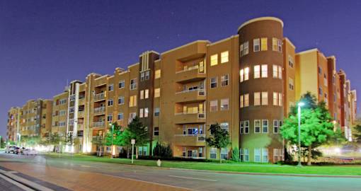 A large apartment building with a curved section on the side is lit up at night.