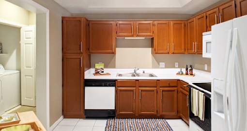 Spacious kitchen with honey brown toned cabinets, white countertops, u-shaped kitchen, and recessed ceiling at Tuscany Lane Apartments in Houston Texas