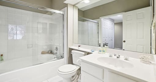Luxury bathroom with white cabinets, cultured marble vanity, and oval soaking tub with glass enclosure at The Saxony Apartments in Dallas