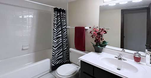 Bathroom with black cabinets, tiled floor, and tiled shower with tub at Kensington Woods Apartments in Omaha Nebraska