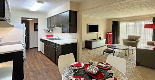 Spacious living room, dining room and kitchen with wood laminate flooring, black cabinets and white countertops at Kensington Woods Apartments