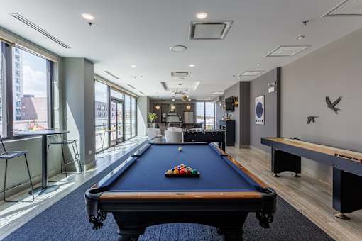 A pool table is in the middle of a room with a bar and a bench.