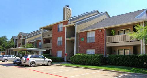 Luxury apartments with red brick exteriors, beautiful landscaping, and spacious balconies at Preston Village Apartments in North Dallas