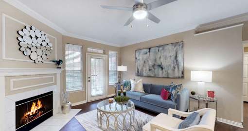 Spacious living room with wood-burning fireplace with glass doors, ceiling fan, French door, at Tuscany Gate Apartments in Houston.