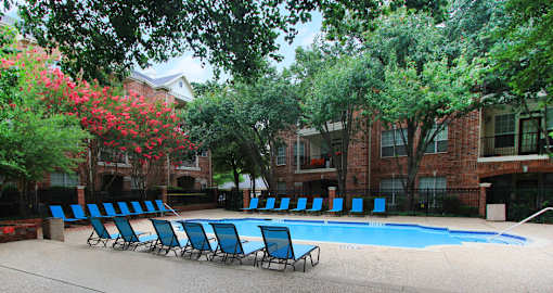 A pool surrounded by trees and chairs.