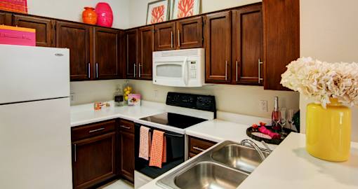 Spacious kitchen with honey brown toned cabinets with modern silver hardware, and white appliances