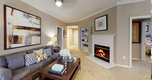 Spacious living room with wood-burning fireplace with glass doors, ceiling fan, crown molding, and built-in bookshelves at Tuscany Apartments in Houston.