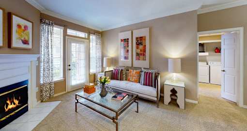 Spacious living room with wood-burning fireplace, French door, crown molding, 9-foot ceilings, full-size washer and dryer, at Tuscany Apartments in Houston.