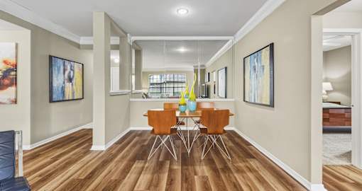 Spacious dining room with wood laminate flooring, large mirror accent wall, decorative crown molding, and gray painted walls Village on the Parkway Apartments