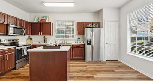 Spacious kitchen with island, wood laminate floor, modern stainless steel appliances, double-sided fridge, lots of cabinet space and extra countertop space, at Village on the Parkway Apartments in Houston Texas
