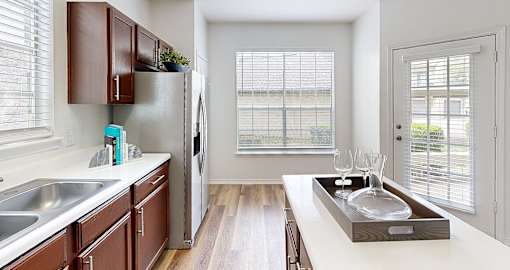 Spacious kitchen with island, wood laminate floor, modern stainless steel appliances, double-sided fridge, lots of cabinet space and extra countertop space, at Village on the Parkway Apartments in Houston Texas