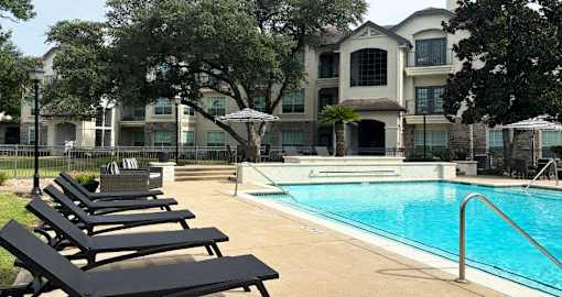 Luxury resort-style swimming pool with fountain, poolside lounges chairs, beautiful landscaping, lush landscaping and scenic views at Village on the Parkway Apartments.